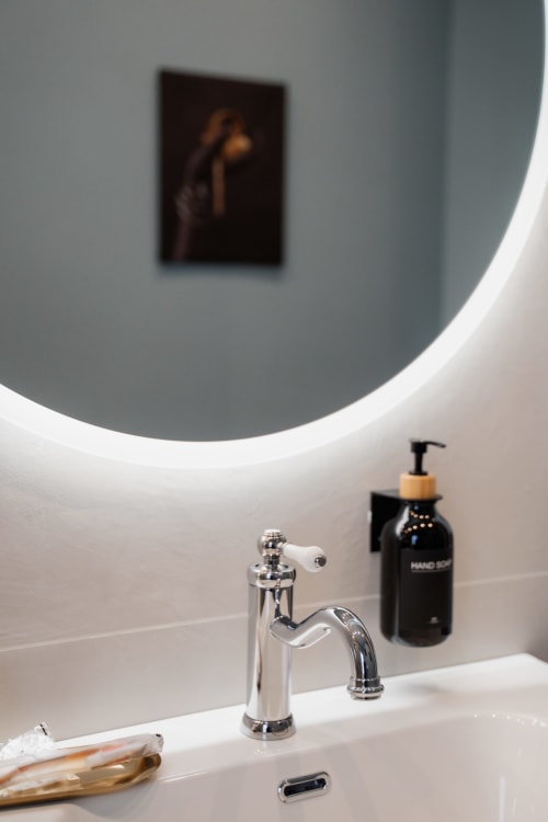 Moderno bagno della Villa Del Sole Inn con specchio rotondo illuminato, rubinetto cromato e dispenser di sapone nero