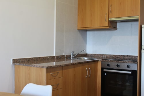 Cocina moderna en Apartamentos Los Gemelos, Foz con muebles de madera, encimera de granito, fregadero y horno empotrado