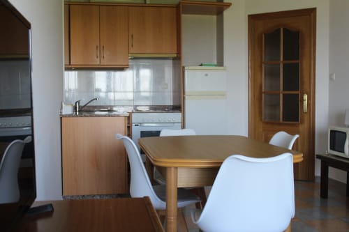 Cocina y comedor modernos en Apartamentos Los Gemelos en Foz con muebles de madera, encimera de granito y sillas blancas