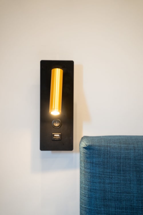 Lampada da lettura moderna a parete con tubo giallo illuminato sopra arredo blu imbottito alla Villa Del Sole Inn,
