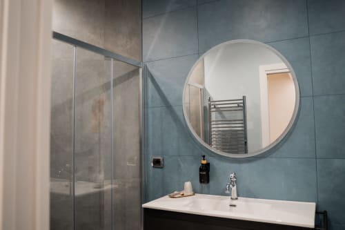 Bagno moderno della Villa Del Sole Inn con specchio rotondo, lavabo bianco, piastrelle turchesi e box doccia in vetro, Campobasso