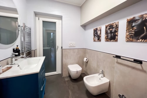 Bagno moderno della Villa Del Sole Inn con lavabo bianco, wc a muro, bidet e decorativa opera d'arte dorata.