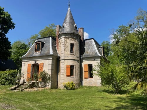 Historic stone château turret with conical roof and orange shutters surrounded by green grounds in Étang sur Arroux, France