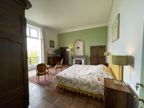 Elegant bedroom at Château de Vaux Morvan with green accent wall, floral bedding, fireplace, and period furniture in Étang