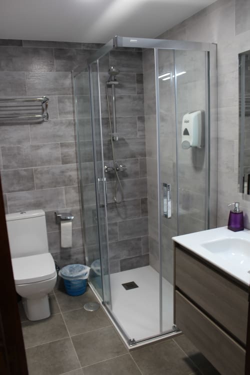 Baño moderno con azulejos grises y mampara de ducha de cristal en el Hotel Rego Foz de Foz, Lugo