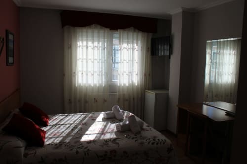 Habitación luminosa del Hotel Rego Foz en Foz, Lugo con camas gemelas, almohadas rojas y luz natural de cortinas translúcidas