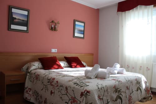 Acogedora habitación del Hotel Rego Foz en Foz con paredes coral, cama de madera, almohadas rojas y edredón floral