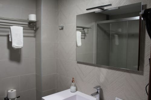 Baño moderno del Hotel Rego Foz en Foz con paredes de azulejos grises, espejo grande, lavabo blanco y accesorios cromados