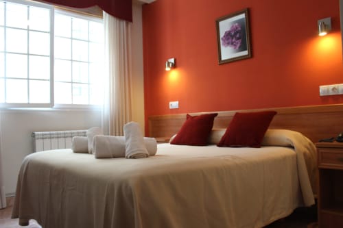 Habitación del Hotel Rego Foz con paredes rojas, cama de madera, ropa de cama beige y almohadas decorativas rojas en Foz, Lugo