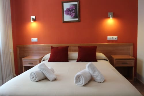 Habitación Hotel Rego Foz con paredes rojas, cama de madera, almohadas burdeos, toallas enrolladas y arte floral enmarcado