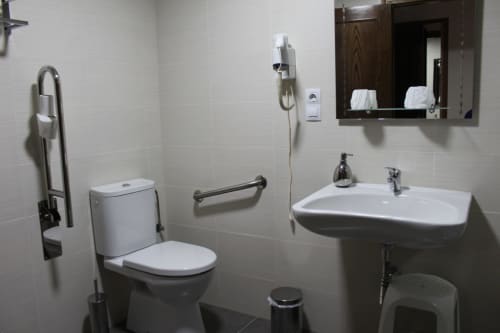 Baño moderno y limpio en Hotel Rego Foz de Foz, Lugo con inodoro, lavabo pedestal, espejo y barras de seguridad