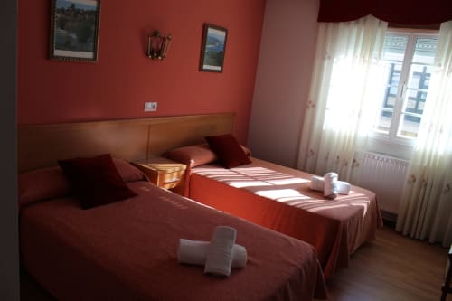Habitación del Hotel Rego Foz con dos camas individuales, ropa de cama burdeos, paredes rojas y grandes ventanales con cortinas translúcidas en Foz, Lugo