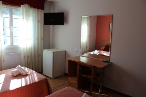 Habitación del Hotel Rego Foz con dos camas individuales, escritorio, espejo, televisor, nevera y ventana en Foz, Lugo