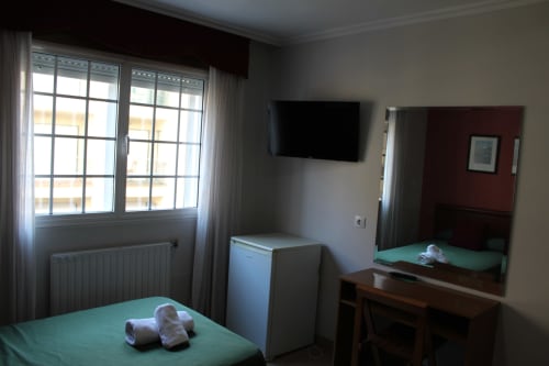 Habitación del Hotel Rego Foz con camas gemelas, TV, espejo, ventana con vista a la ciudad y amenidades blancas