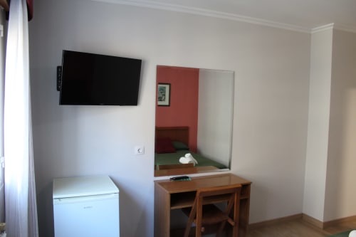 Habitación del Hotel Rego Foz con TV mural, escritorio, espejo, minibar y pared de acento rojo en Foz, Lugo