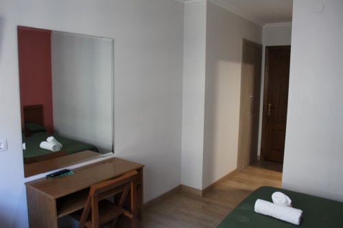Habitación del Hotel Rego Foz con escritorio de madera, espejo, ropa de cama verde y toallas blancas en Foz, Lugo