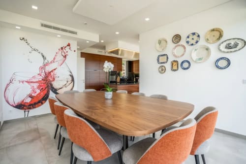 Sala de jantar moderna da Casa Da Colina com mesa de madeira, cadeiras laranjas, arte com respingo de vinho e pratos decorativos em branco
