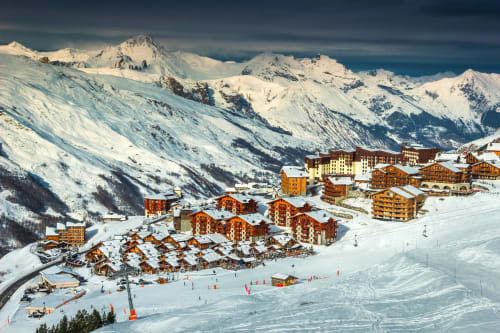 Aerial view of Brides-les-Bains ski resort with wooden chalets, snow-covered slopes, and alpine peaks in background.