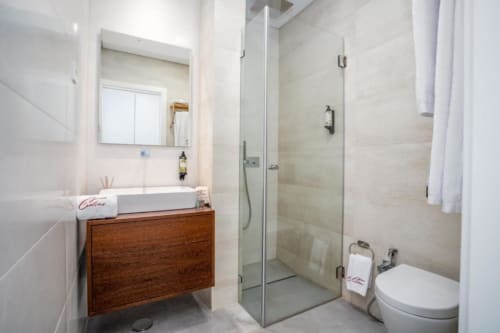 Banheiro moderno da villa Casa da Colina com pia branca, gabinete de madeira, box de vidro e vaso sanitário