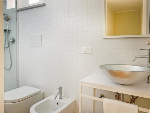 Bagno moderno con piastrelle bianche, lavabo da appoggio, WC e cabina doccia in vetro presso Residence Balconi del Conero