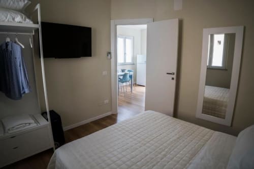 Modern bedroom in Marcelli apartment with white bed, TV, mirrored wardrobe, and open-plan kitchen and living area beyond