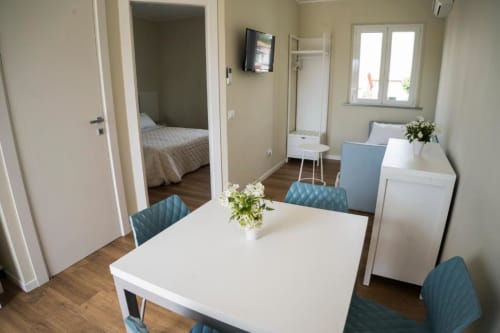 Modern apartment living area with dining table, blue chairs, wooden flooring, and open bedroom at Residence Balconi del