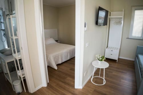 Modern apartment living area with bedroom, white furniture, wooden flooring, TV, and round side table at Residence Balconi