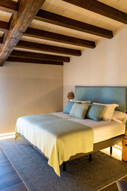 Habitación luminosa en Casa Rural San Andres de Teixido con vigas de madera vistas, cama con cabecero azul y ropa de cama amarilla