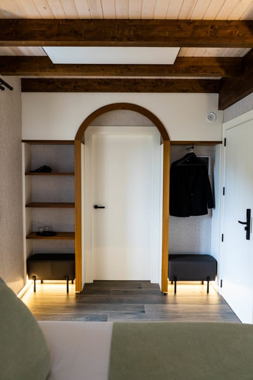 Entrada de dormitorio moderno con puerta arqueada de madera, estanterías empotradas y perchero oscuro en Casa Rural San Andres de Teixido