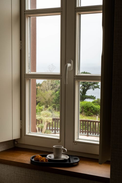 Vista al mar desde la ventana de Casa Rural San Andrés de Teixido con taza de café y pastel en el alféizar de madera