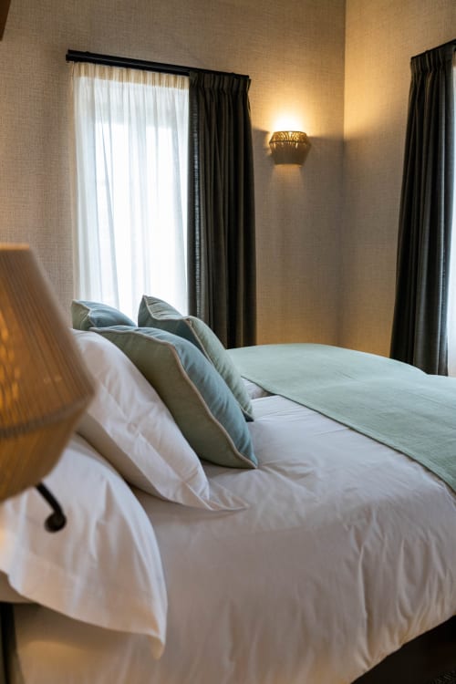 Dormitorio moderno en Casa Rural San Andrés de Teixido con vistas al mar, sábanas blancas, almohadas verdes y cortinas oscuras