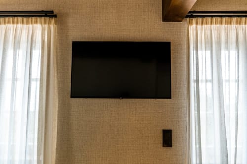 Televisor LED montado en pared en moderno dormitorio con paredes texturizadas beige y cortinas traslúcidas crema en Casa Rural San Andres de