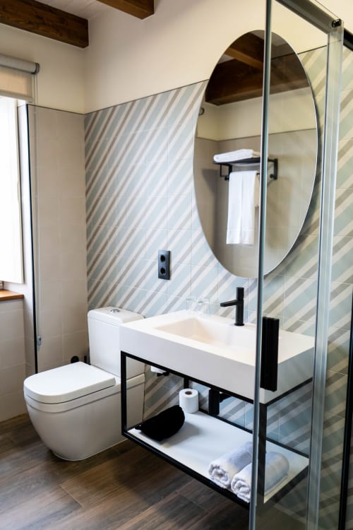 Baño moderno con espejo ovalado, lavamanos blanco, grifería negra y azulejos a rayas en Casa Rural San Andrés de Teixido, Galicia