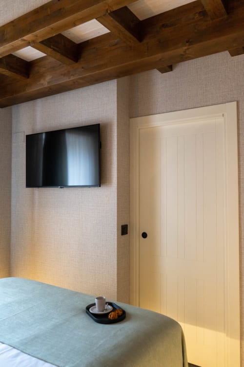Dormitorio moderno en Casa Rural San Andres de Teixido con televisor de pared, vigas de madera, puerta crema y mesa con