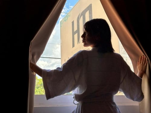 Huésped abriendo las cortinas de la habitación del Hotel Makarios en Tuxtla Gutiérrez, con vista a la ciudad y edificio amarillo afuera