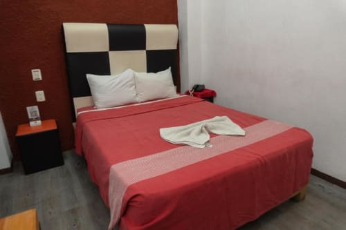 Habitación del Hotel Makarios en Tuxtla Gutiérrez con ropa de cama roja, cabecera a cuadros blanco y negro, y muebles modernos