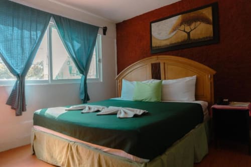 Habitación del Hotel Makarios en Tuxtla Gutiérrez con cama de madera, ropa de cama verde, cortinas turquesas y decoración en tonos tierra