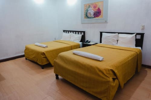 Habitación del Hotel Makarios en Tuxtla Gutiérrez con dos camas, ropa de cama amarillo dorado, almohadas blancas y cuadros florales