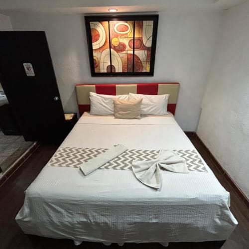 Habitación moderna del Hotel Makarios en Tuxtla Gutiérrez con cama queen, cabecero rojo y crema, y arte geométrico en la pared.