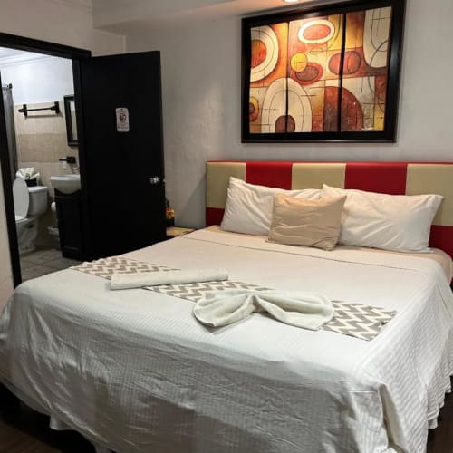 Habitación del Hotel Makarios en Tuxtla Gutiérrez con cama de cabecera roja y beige, almohadas blancas, acceso al baño y cuadro decorativo