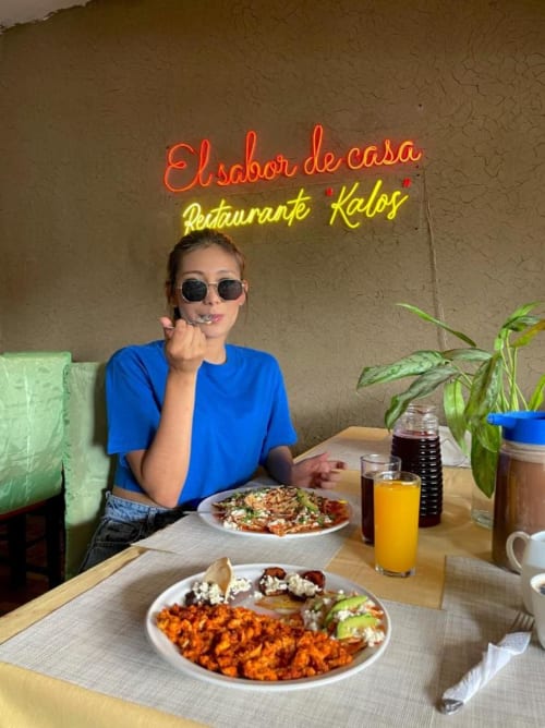 Mujer disfrutando de una comida en el restaurante El sabor de casa en Tuxtla Gutiérrez con platillos coloridos y letrero de neón