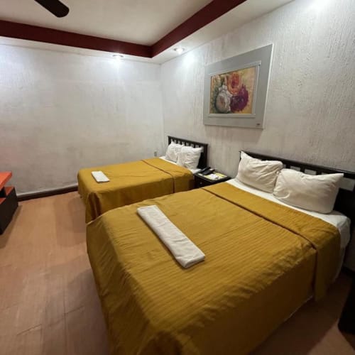 Habitación del Hotel Makarios en Tuxtla Gutiérrez con dos camas, ropa de cama amarilla, almohadas blancas, cuadros decorativos y diseño moderno de techo