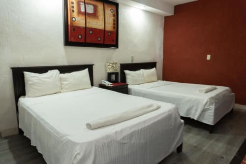 Camas dobles en Hotel Makarios, Tuxtla Gutiérrez con sábanas blancas, cabeceros negros y pared de acento rojo