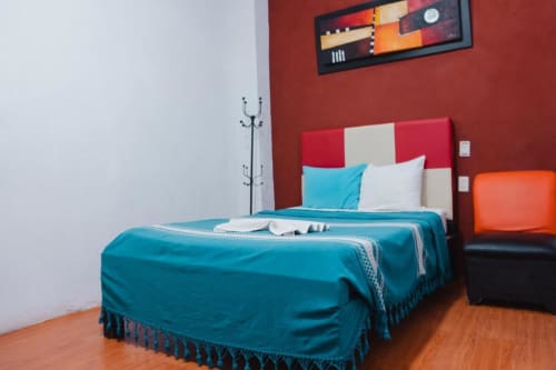 Habitación moderna del Hotel Makarios en Tuxtla Gutiérrez con ropa de cama turquesa, cabecero rojo y crema, y diseño contemporáneo