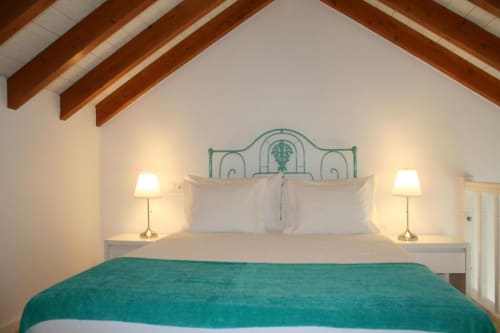 Bright bedroom at Recantus Comporta with turquoise headboard, exposed wooden beams, white bedding, and bedside lamps