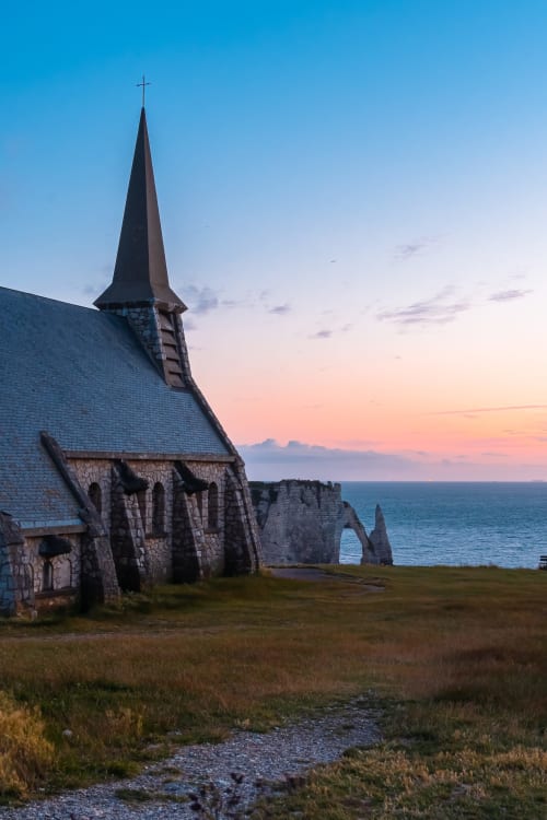 Historic stone chapel at sunset overlooking Étretat cliffs and ocean, Villa Eliane nearby