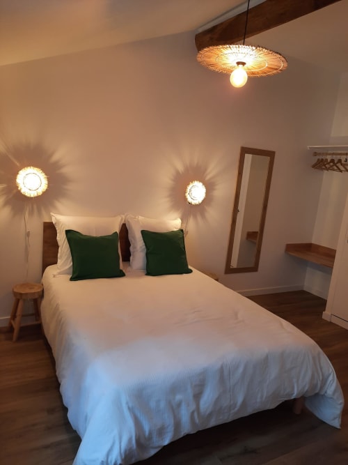 Chambre de Maison Rinette à Dijon avec literie blanche, oreillers verts, accents en bois et éclairage mural ambiant