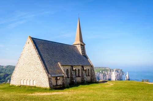 Historic stone chapel with tall spire overlooking white limestone cliffs and ocean in Étretat, France