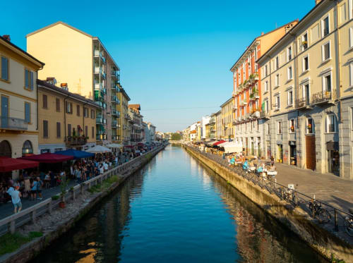 Canal Navigli à Milan avec bâtiments historiques colorés, restauration en terrasse et ciel bleu dégagé