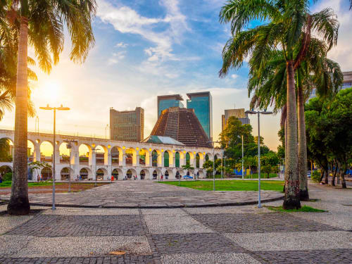 Lapa Aqueduct with palm trees and modern Rio de Janeiro skyline at sunset, iconic landmark near Rio Vibes Hostel